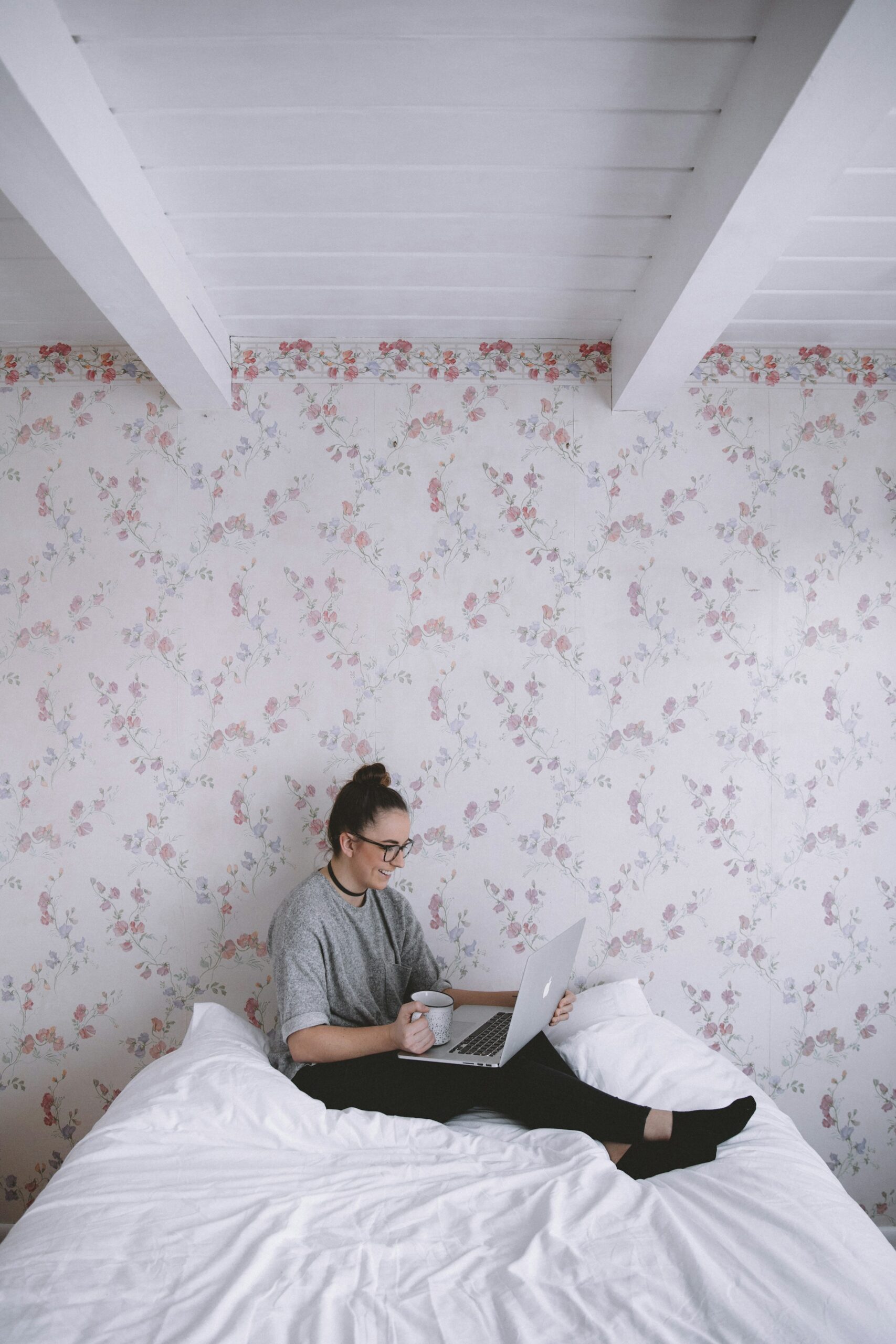 Girl Sitting On Bed Working On Her Laptop with a floral wallpaper